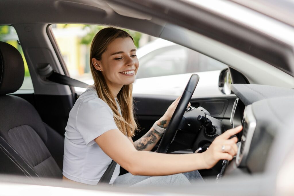 Young woman adjusting car radio while driving modern vehicle